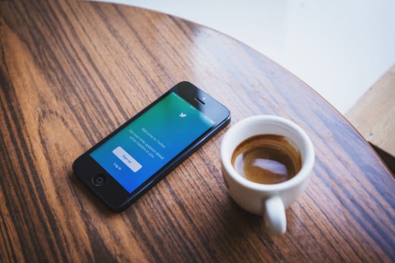 Smartphone showing a Twitter sign-up screen resting on a wooden table beside a cup of espresso